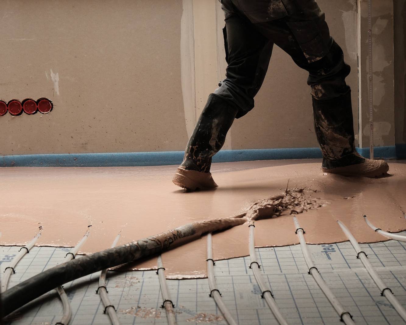 Einbau von STANIplan-Fließestrich aus einem Schlauchsystem, dabei sind die Schuhe eines Mitarbeiters im Bild zu sehen.
