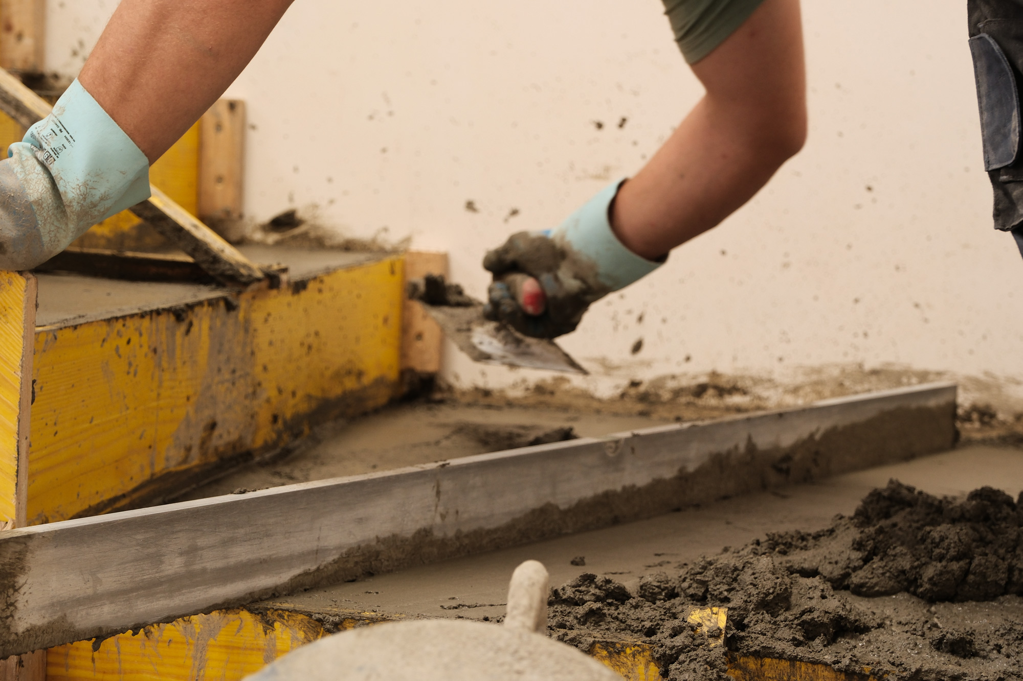 Nahaufnahme eines Mitarbeiters beim EInbau von Zementestrich auf Treppenstufen.