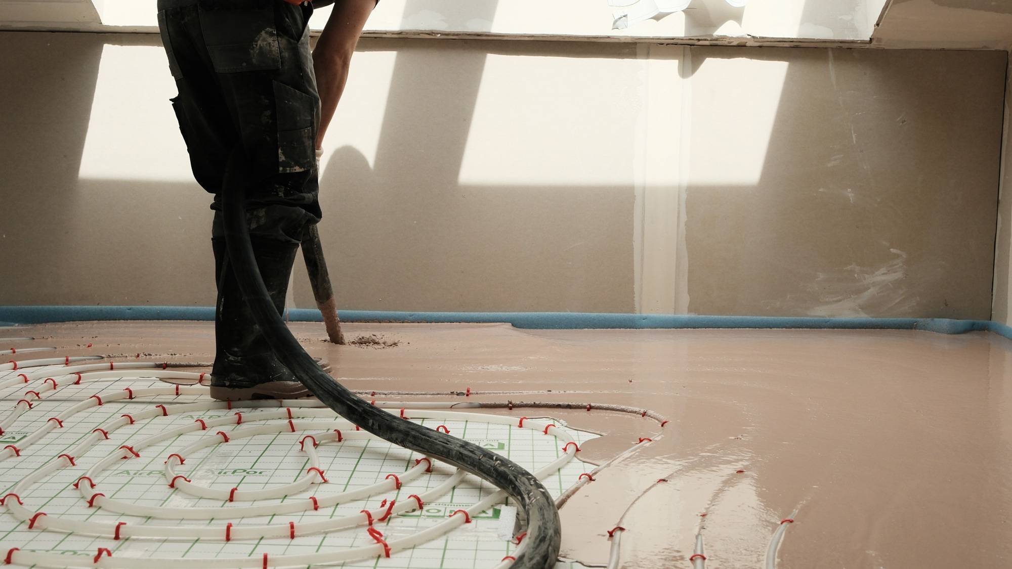 Mitarbeiter beim Einbau von STANIplan Eigenkonstruktion mit Schlauch auf einer Baustelle &uuml;ber der Fu&szlig;bodenheizung.