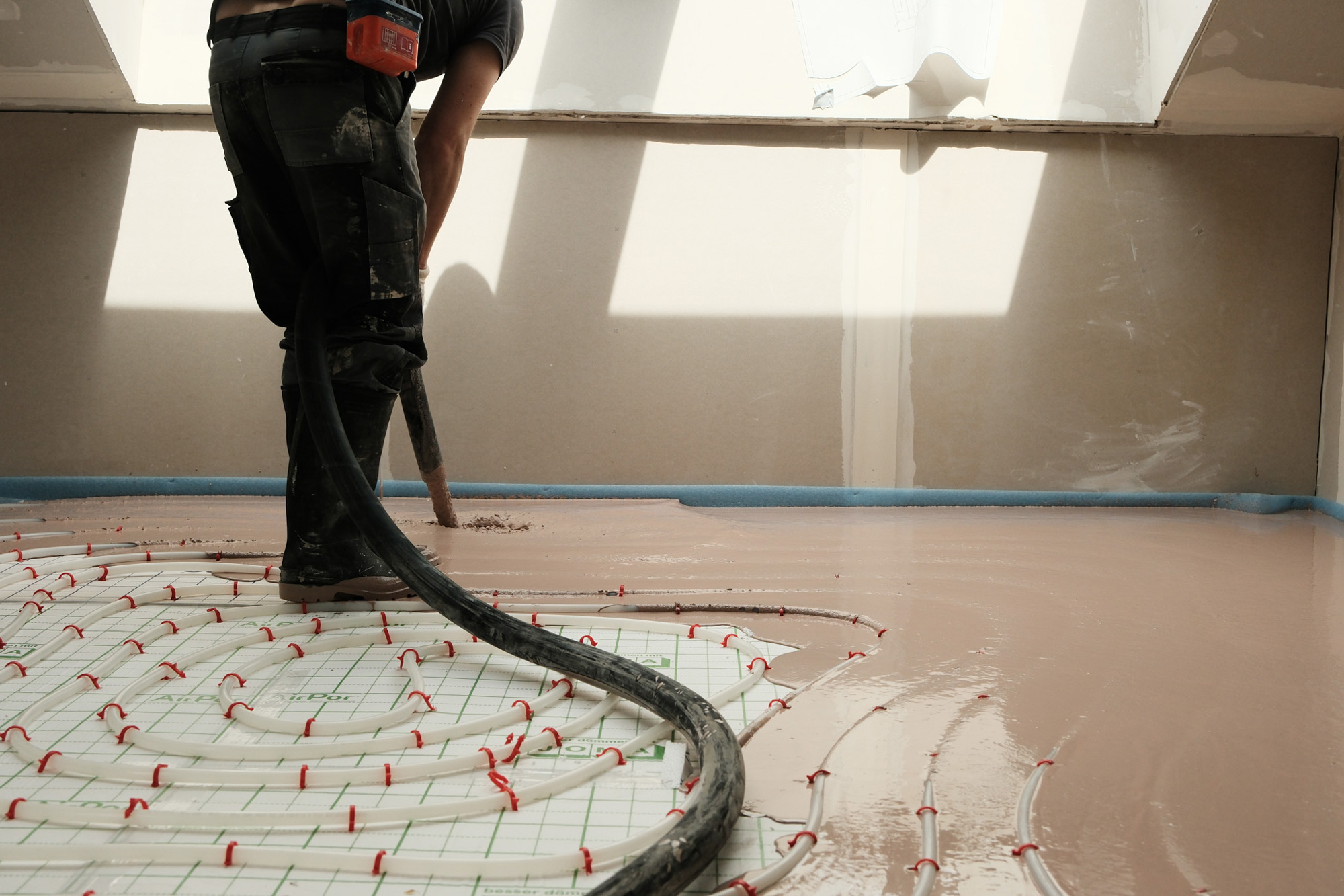 Mitarbeiter beim Einbau von STANIplan Eigenkonstruktion mit Schlauch auf einer Baustelle über der Fußbodenheizung.